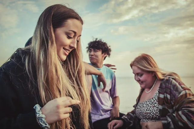 Three young people laughing together by the water at sunset.